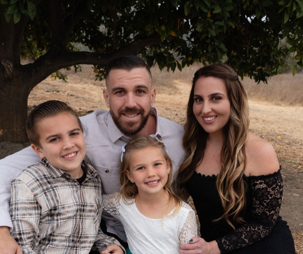 The family behind DaycareSuite: Glenn and Maryam Fraser with their two children, sitting together outdoors under a tree